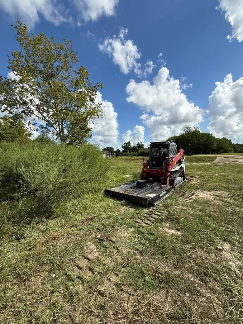 Skid steer with a brush cutter attachment working the open field next to a brush line on the West Houston property.
